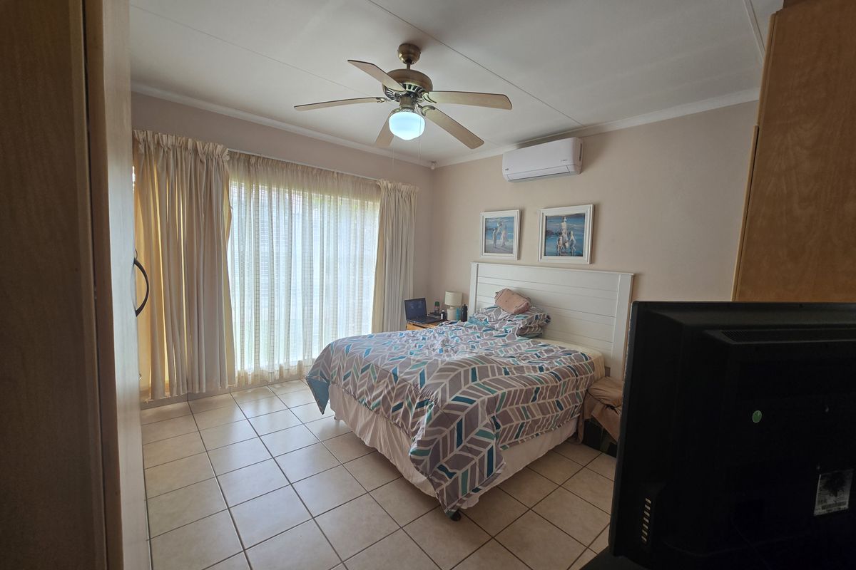 A bedroom featuring tiled flooring, a ceiling fan, and a wall-mounted split-system air conditioner, with direct access to an outdoor area via sliding doors.