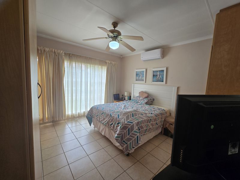 A bedroom featuring tiled flooring, a ceiling fan, and a wall-mounted split-system air conditioner, with direct access to an outdoor area via sliding doors.