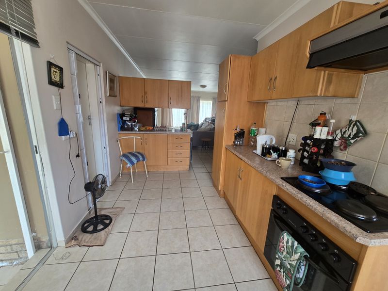 A functional kitchen featuring light wood cabinetry, laminate countertops, tiled flooring, and integrated cooking appliances, offering a practical layout for daily use.