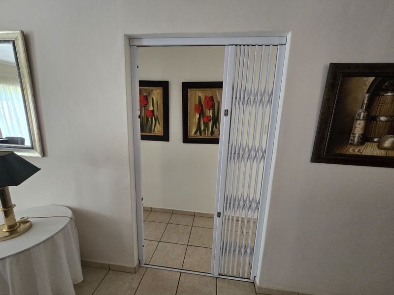 A hallway featuring tiled flooring and a white retractable security gate providing access to an adjacent area.