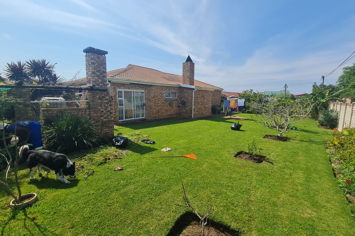 A spacious rear garden featuring a well-maintained lawn, brick chimney, and tiled roof facade with sliding door access.