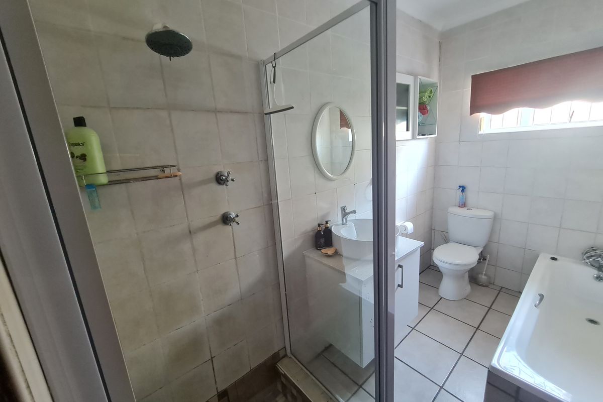 A functional bathroom featuring a separate shower enclosure, bathtub, vanity basin, and toilet with neutral wall and floor tiling.