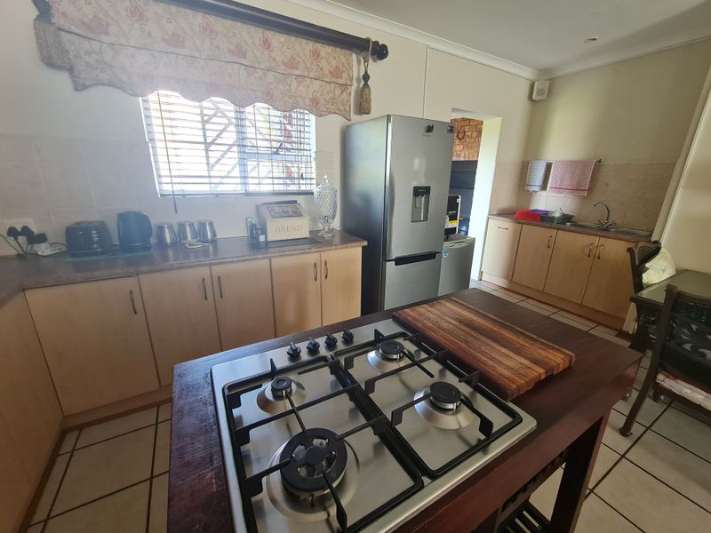 A functional kitchen featuring a central island with a gas hob, ample cabinetry, laminate countertops, and tiled flooring.