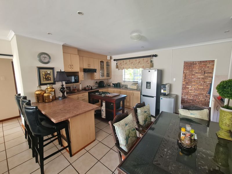 Open-plan kitchen and dining area featuring light wood cabinetry, laminate countertops, gas hob, tiled flooring, and a decorative exposed brick wall.