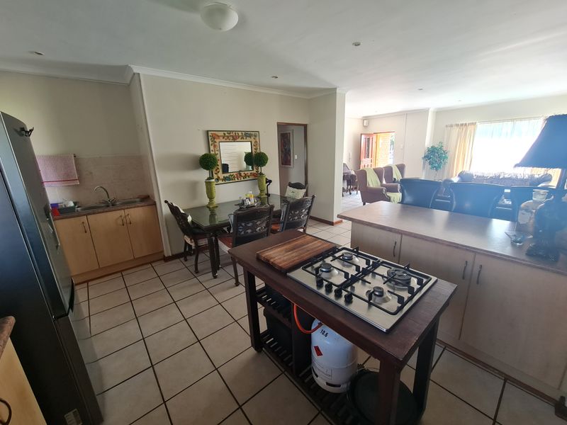 Open-plan kitchen and dining area featuring tiled flooring, wooden cabinetry, a central island with a gas hob, and integrated lighting.