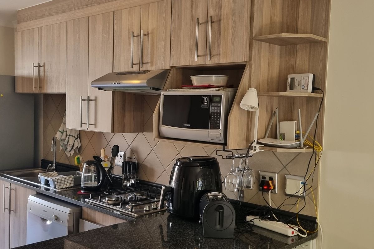 A functional kitchen featuring wood-look cabinetry, granite countertops, a gas hob, and an integrated extractor fan with a tiled backsplash.