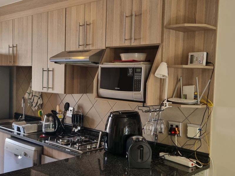 A functional kitchen featuring wood-look cabinetry, granite countertops, a gas hob, and an integrated extractor fan with a tiled backsplash.
