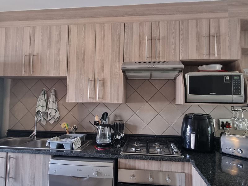 A functional kitchen featuring light wood-grain cabinetry, dark granite countertops, a gas hob, built-in oven, and a tiled backsplash.