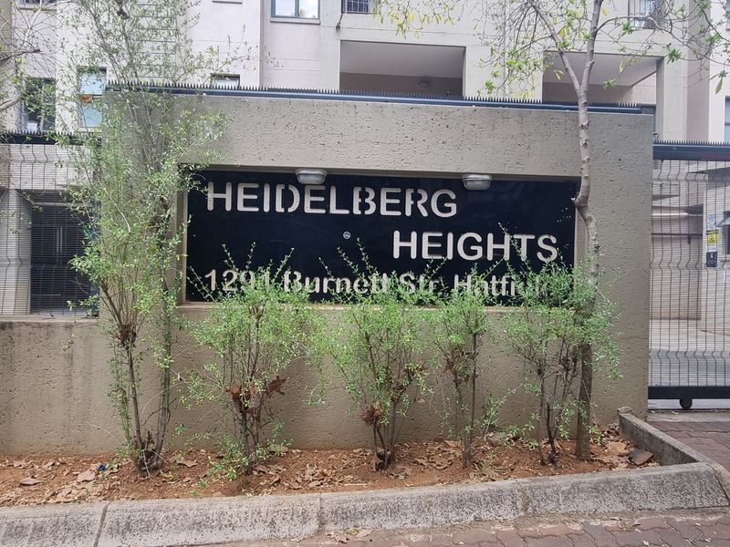 The front entrance and security gate of the Heidelberg Heights apartment complex, featuring clear building signage and paved access.