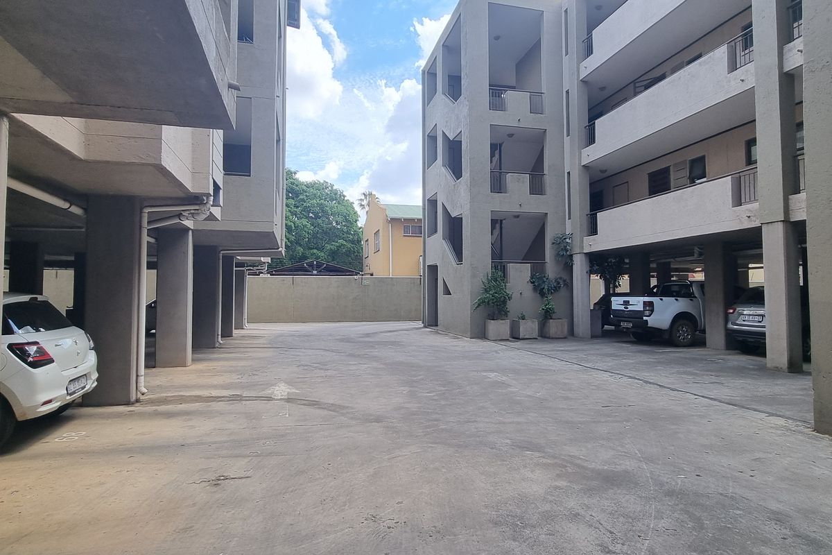 View of the apartment complex exterior showing the covered parking area, concrete structural pillars, and building facade with balconies.