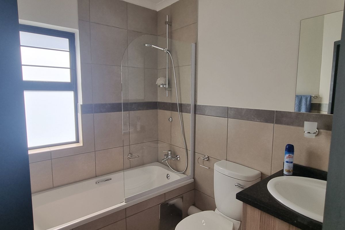 A clean, functional bathroom featuring a bathtub with a glass shower screen, a vanity with a basin, and neutral wall tiling.