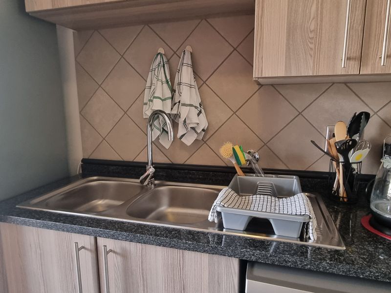 A functional kitchen area featuring a double bowl stainless steel sink, granite countertops, tiled backsplash, and wood-finish cabinetry.
