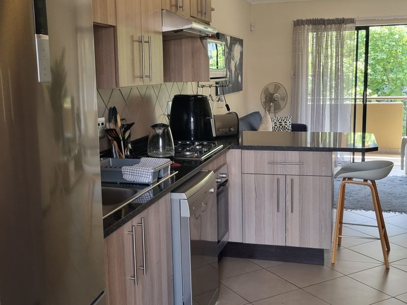 Open-plan kitchen featuring modern wood-finish cabinetry, granite countertops, and integrated appliances, flowing seamlessly into the living area with access to a balcony.