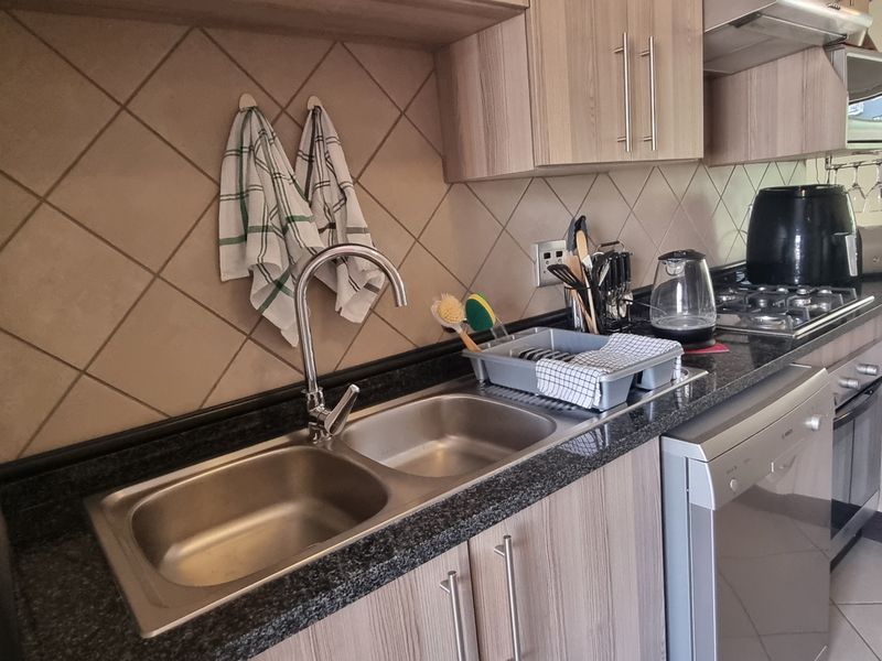 A functional kitchen featuring granite countertops, a double bowl stainless steel sink, built-in cabinetry, and integrated appliances including a gas hob and oven.