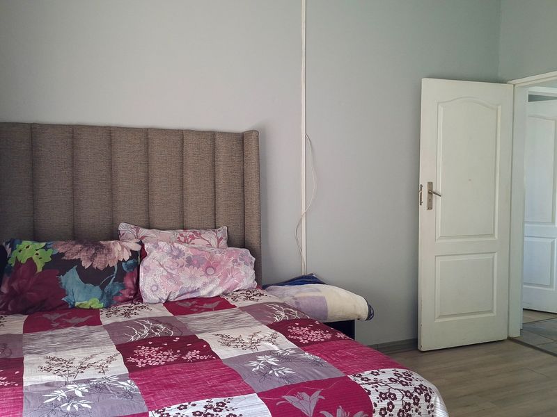 A bedroom featuring laminate flooring and a standard panel door, with visible surface-mounted electrical wiring requiring attention.