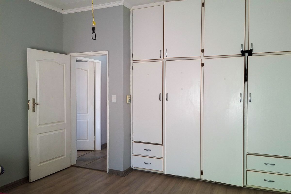 A bedroom featuring extensive built-in white cabinetry, laminate flooring, and neutral wall tones, offering a functional and clean space ready for personalization.