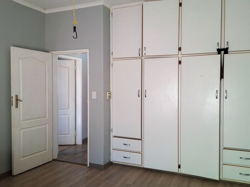 A bedroom featuring extensive built-in white cabinetry, laminate flooring, and neutral wall tones, offering a functional and clean space ready for personalization.