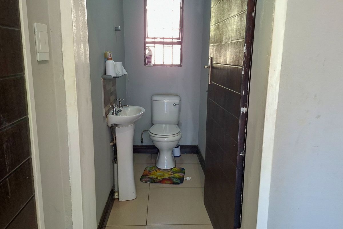 A compact guest bathroom featuring a pedestal basin, toilet, and tiled flooring, with a window providing natural light.