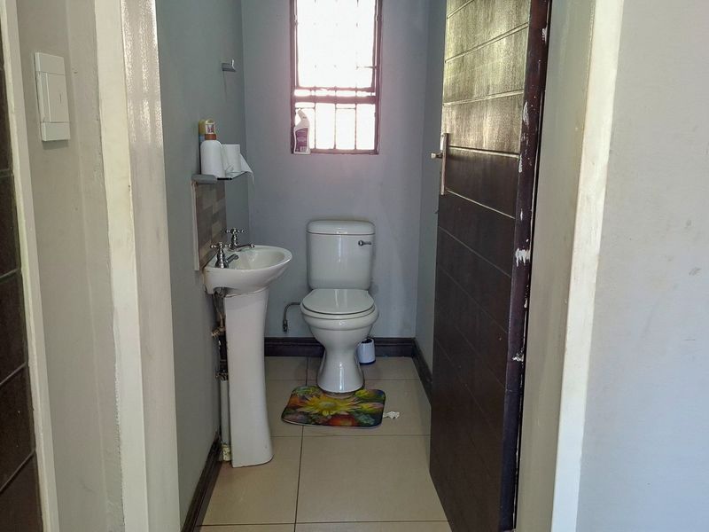 A compact guest bathroom featuring a pedestal basin, toilet, and tiled flooring, with a window providing natural light.