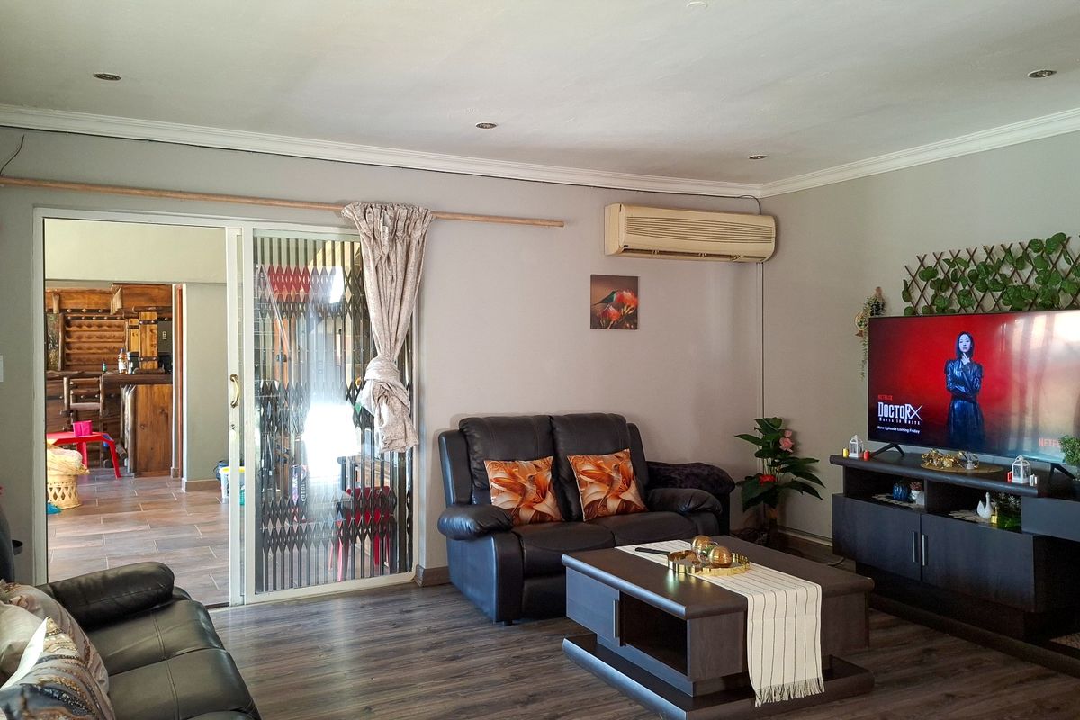 A comfortable living room featuring laminate flooring, recessed lighting, and a sliding glass door with security gate leading to an adjacent space.