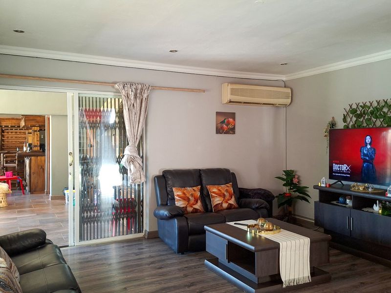 A comfortable living room featuring laminate flooring, recessed lighting, and a sliding glass door with security gate leading to an adjacent space.