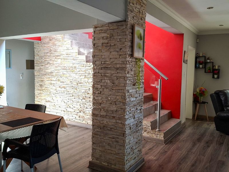 Open plan living and dining area featuring a prominent stone-clad feature pillar, stone-accented staircase wall, and modern laminate flooring.