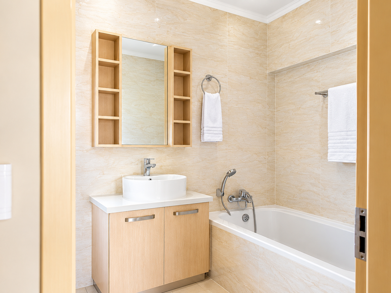 Modern bathroom featuring a light wood vanity with vessel sink, integrated shelving, and a bathtub with tiled wall finishes.