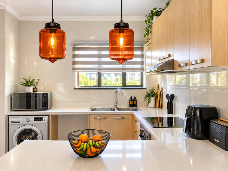 Modern kitchen featuring light wood cabinetry, quartz countertops, integrated appliances, and stylish pendant lighting, offering a clean and functional workspace.