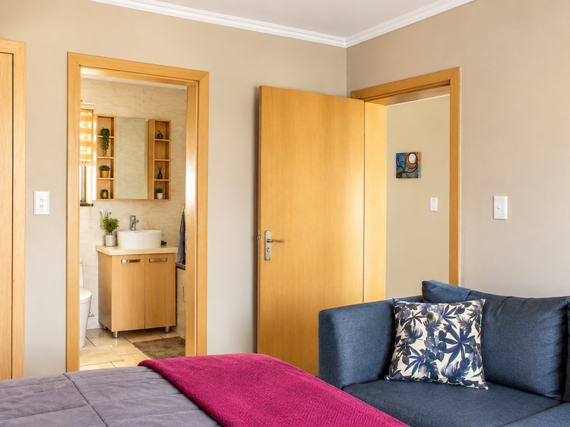 A well-maintained bedroom featuring wooden door frames, coving, and direct access to an en-suite bathroom with modern vanity.