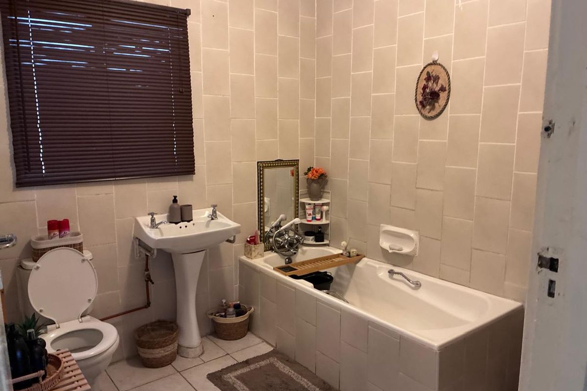 A dated bathroom featuring a pedestal basin, built-in bathtub, and full-height wall tiling, offering significant potential for a modern renovation.