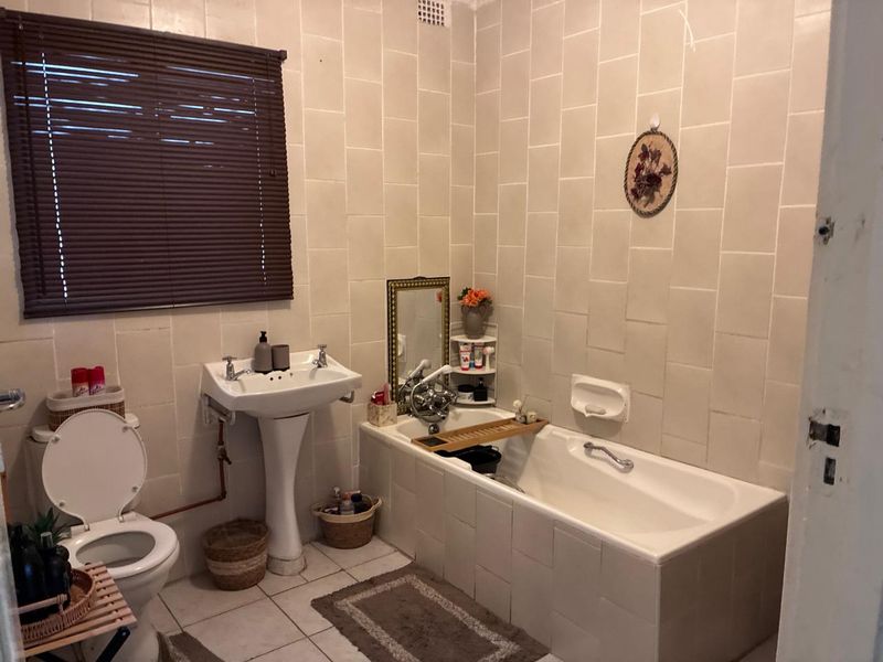 A dated bathroom featuring a pedestal basin, built-in bathtub, and full-height wall tiling, offering significant potential for a modern renovation.