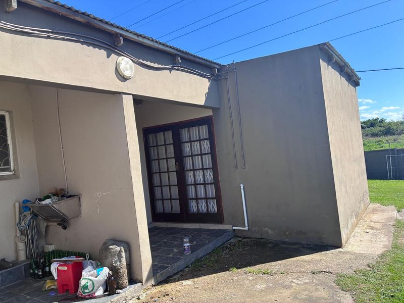 Rear exterior view of the property featuring a covered patio area, double glass doors, and exposed exterior plumbing and electrical conduits.