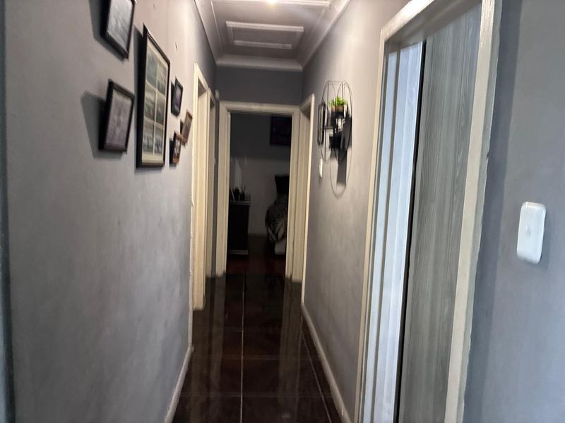 A narrow residential hallway featuring dark tiled flooring, coved ceilings, and recessed lighting, providing access to multiple rooms.