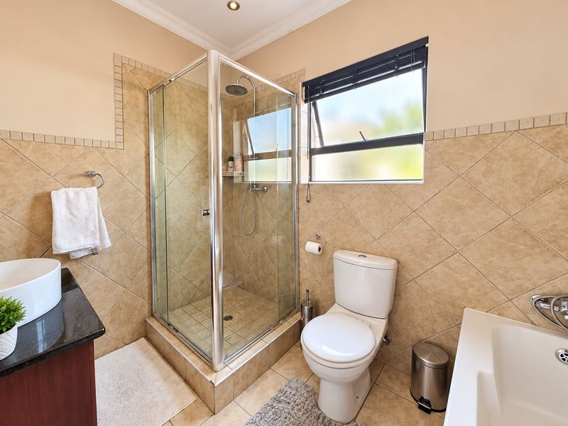 A functional bathroom featuring a glass-enclosed shower, a modern vanity basin, and neutral-toned wall and floor tiling.