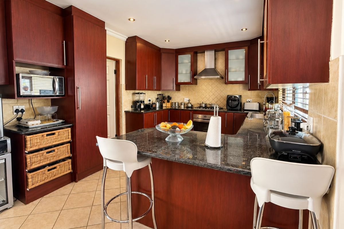 A well-maintained kitchen featuring dark wood cabinetry, granite countertops, a central breakfast island, and integrated appliances with neutral tiled finishes.