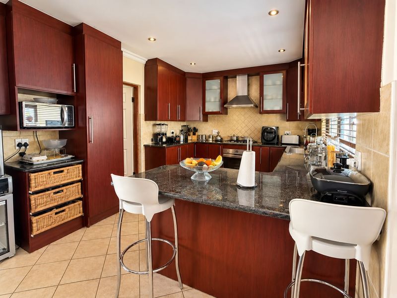 A well-maintained kitchen featuring dark wood cabinetry, granite countertops, a central breakfast island, and integrated appliances with neutral tiled finishes.
