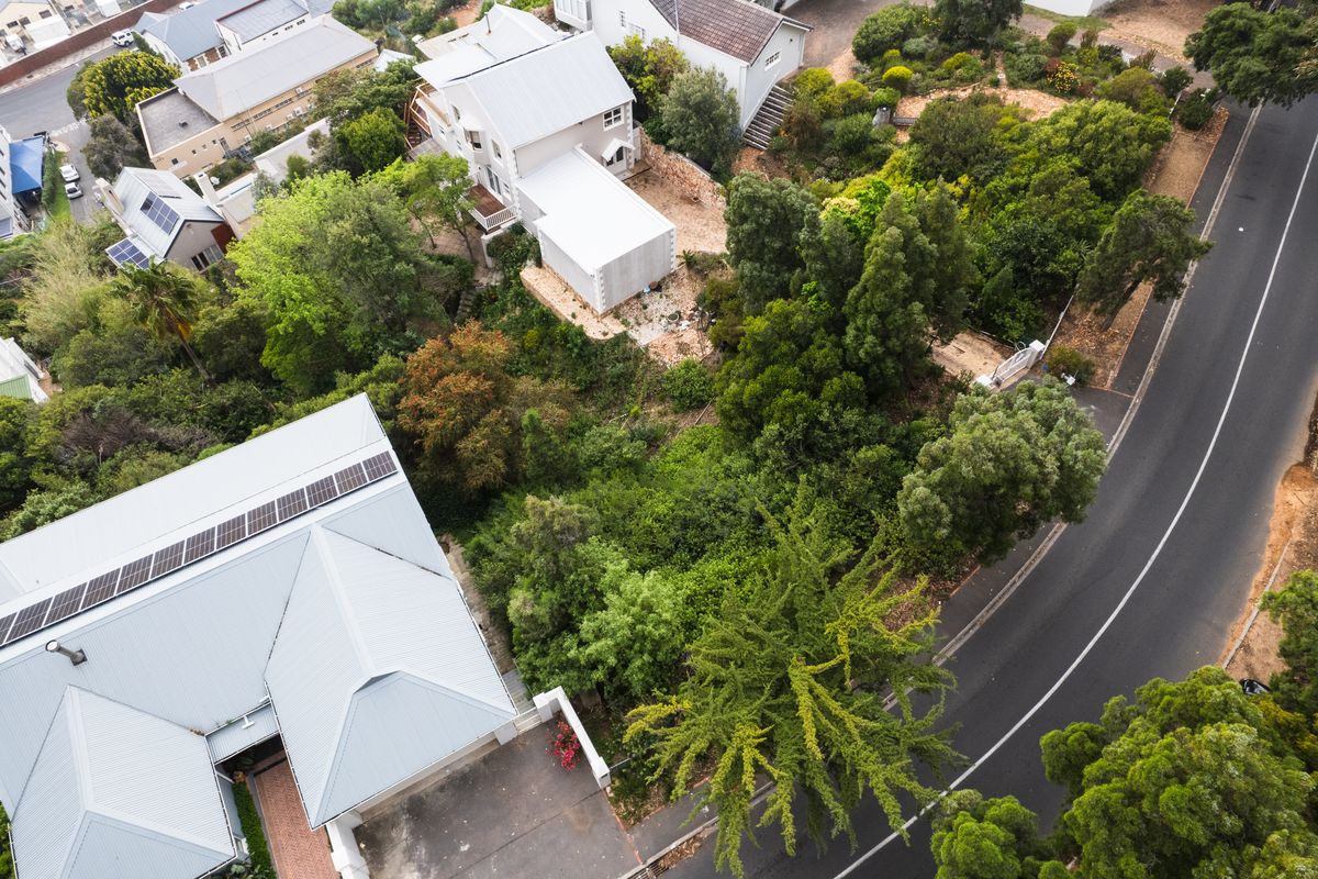Aerial view of a residential property featuring mature landscaping, a paved driveway, and a building with solar panels installed on the roof.