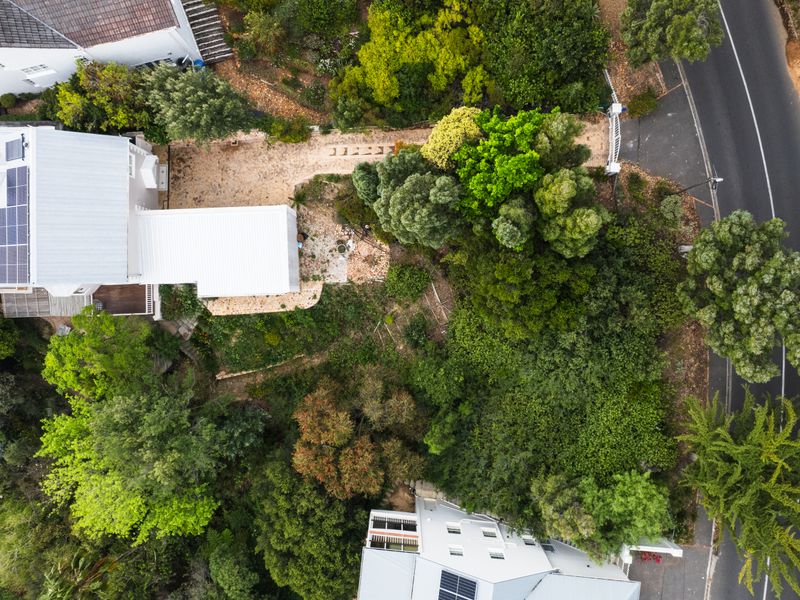 Aerial view of a residential property featuring a paved driveway, mature garden landscaping, and solar panels installed on the roof.