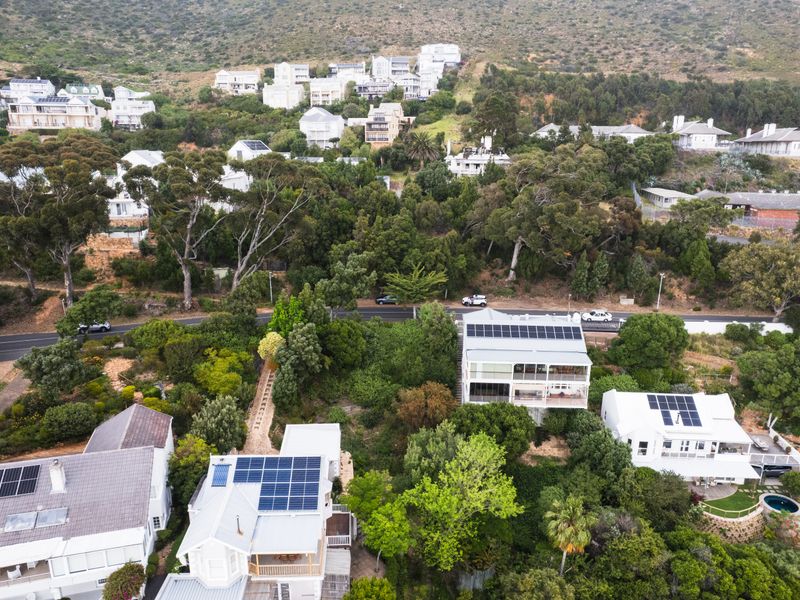 An aerial view of a residential neighborhood featuring homes with solar panel installations, surrounded by lush greenery and mature trees.