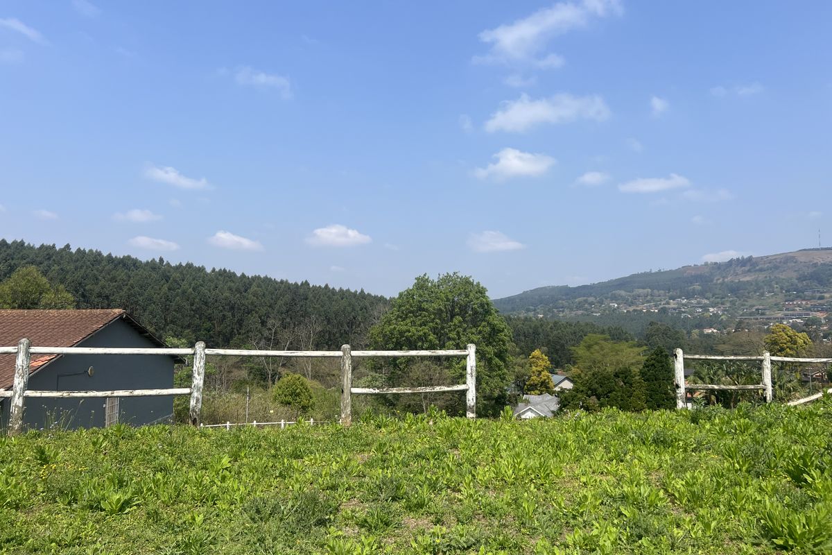 A scenic view overlooking a green landscape with a forest and distant hills, framed by a white post and rail fence.