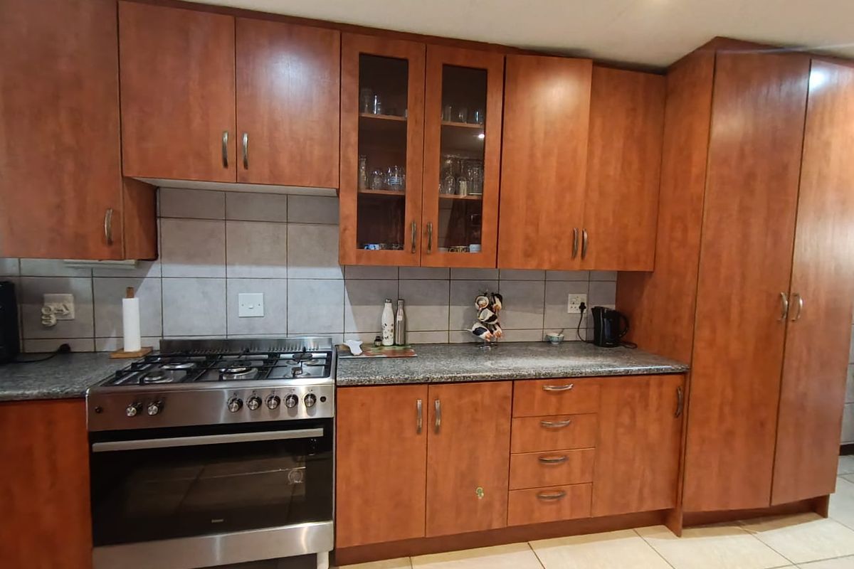 A functional kitchen featuring wood-finish cabinetry, granite countertops, a gas stove with oven, and tiled flooring.