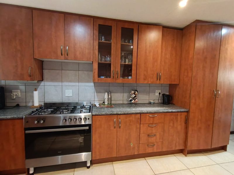 A functional kitchen featuring wood-finish cabinetry, granite countertops, a gas stove with oven, and tiled flooring.
