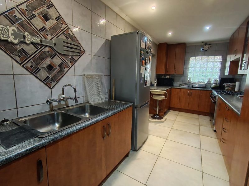 A functional kitchen featuring wooden cabinetry, laminate countertops, a double bowl sink, tiled splashbacks, and a distinctive glass block window.