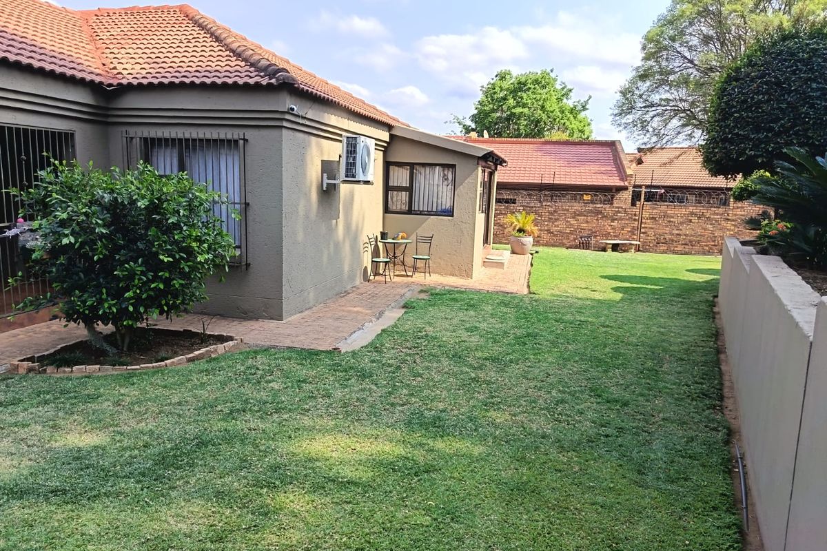 Rear view of the house featuring a well-maintained lawn, paved walkway, and secure boundary wall.