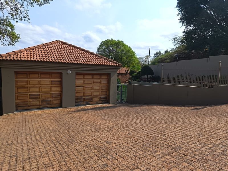 A double garage with wooden doors and a tiled roof, featuring a paved driveway and secure boundary walling.