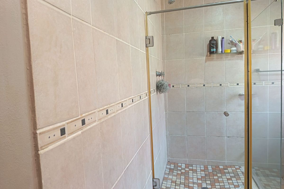 A functional bathroom shower area featuring neutral ceramic wall tiles, a mosaic tiled floor, and a glass shower enclosure with gold-toned framing.