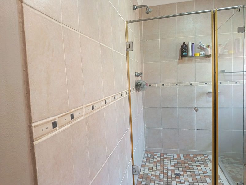 A functional bathroom shower area featuring neutral ceramic wall tiles, a mosaic tiled floor, and a glass shower enclosure with gold-toned framing.