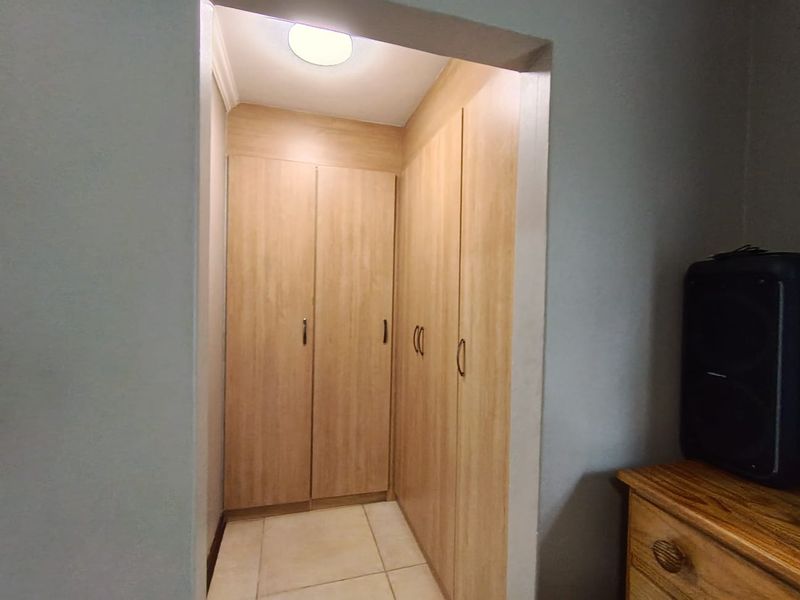 A functional hallway featuring extensive built-in wooden cabinetry for storage, tiled flooring, and a clean, neutral aesthetic.