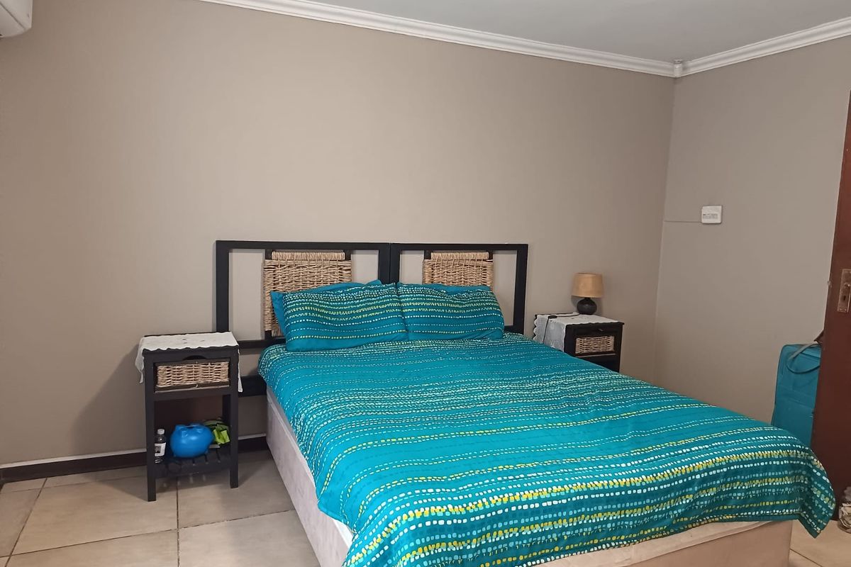 A functional bedroom featuring tiled flooring, coved cornicing, and a wall-mounted air conditioning unit.