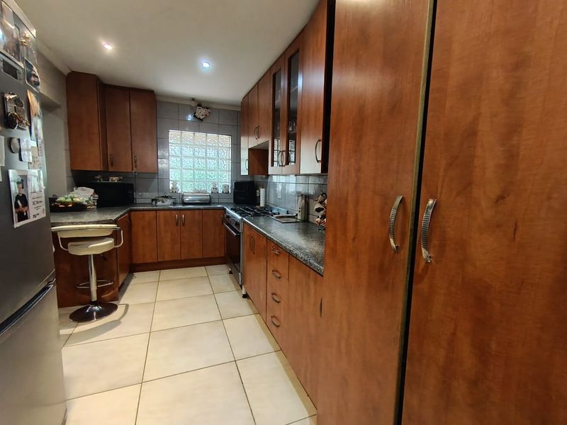 A functional kitchen featuring warm-toned laminate cabinetry, granite countertops, a glass block window, and built-in cooking appliances with tiled flooring.